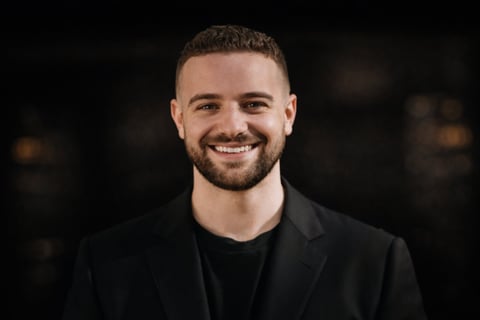 Smiling man with beard wearing black blazer and shirt against dark background