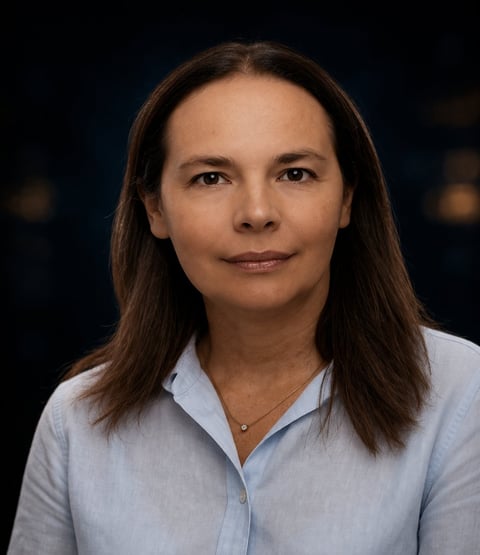 Professional headshot of a woman with long brown hair wearing a light blue button-up shirt against a dark background