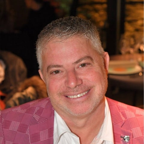 Middle-aged man with gray hair smiling at camera, wearing pink plaid blazer and white shirt